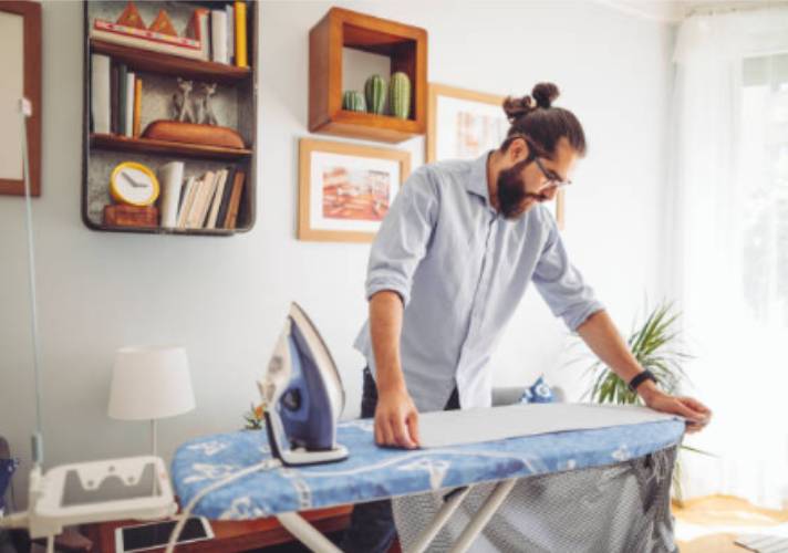 A man placing his clothes on the ironing board